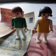 Zwei Playmobilfiguren auf Geldscheinen.
