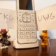 Zwei Lego-Figuren halten Schilder mit "TKG" und "UWG" hoch und stehen neben einem Telefon.